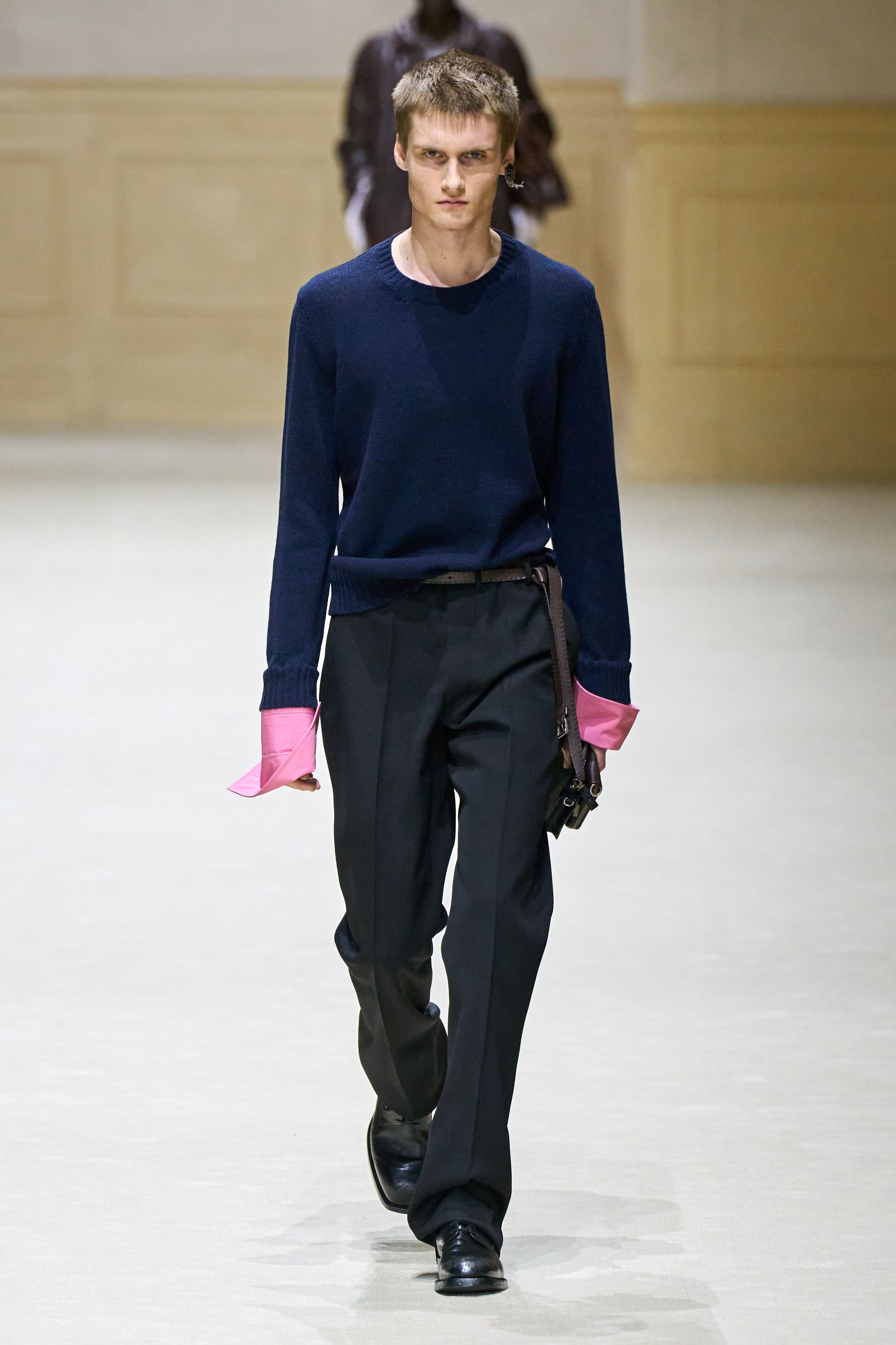 Prada 2026秋冬继续以“制服感”为切入口，重构男性权力与脆弱性的关系。修身西装、直筒大衣与功能性外套在高度理性的廓形中出现，却通过红色针织、围巾与内搭打破秩序。系列在严肃与松动之间反复摇摆，呈现一种当代男性在社会角色与个体情绪之间的张力。这是Prada一贯的冷静叙事，也是其思想性持续领先的关键简-顽石频道趋势研究
